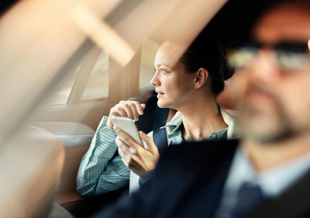 A woman sitting in the back of a car holding her phone.