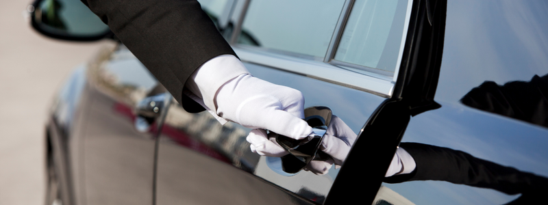 A person in white gloves holding onto the door handle of a car.